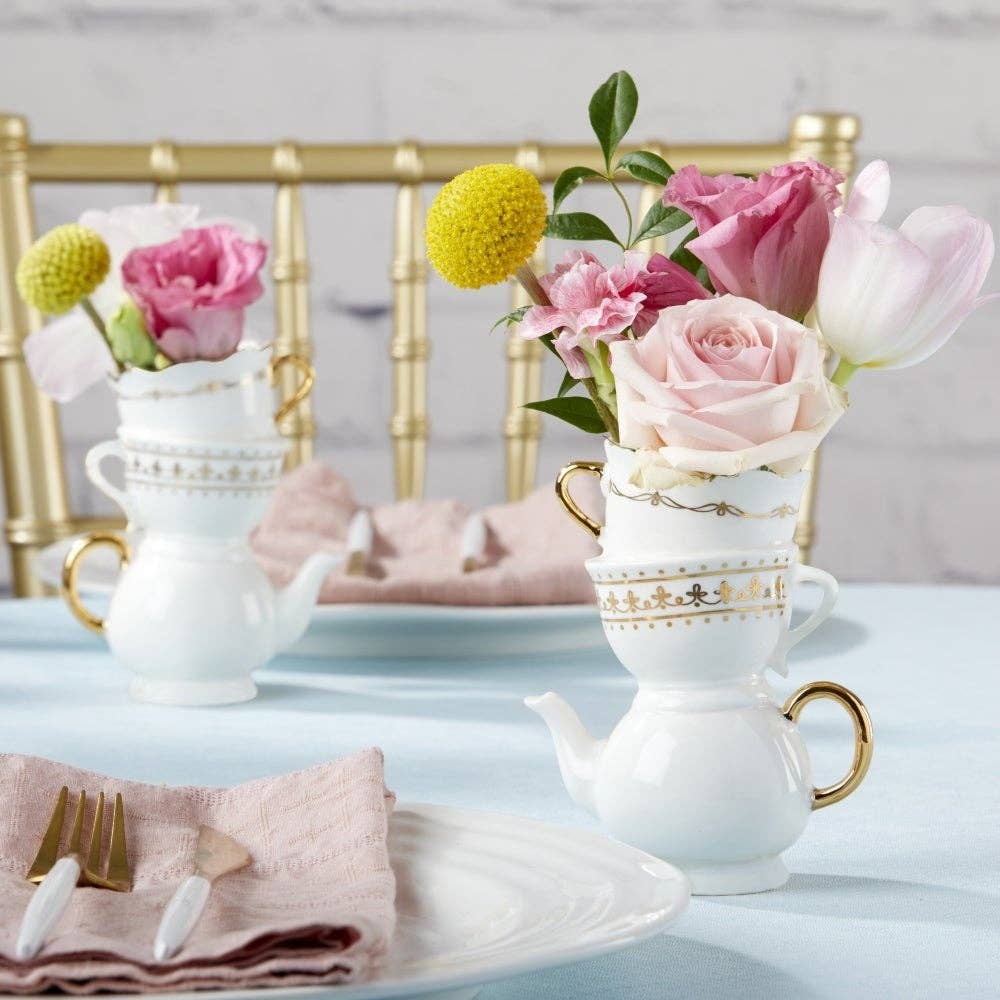Teacups with floral arrangements on a table setting with pink napkins and gold cutlery.