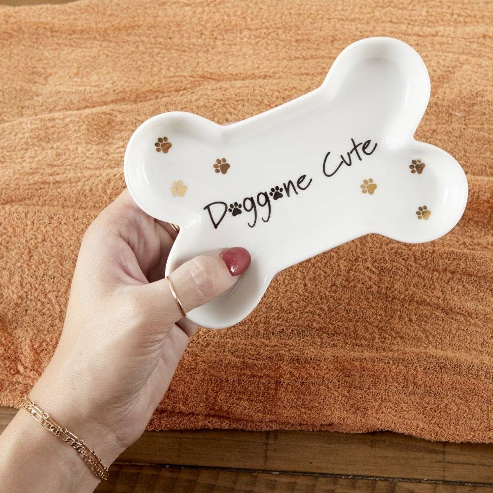 Hand holding a bone-shaped tray with 'Doggone Cute' text on a wooden surface