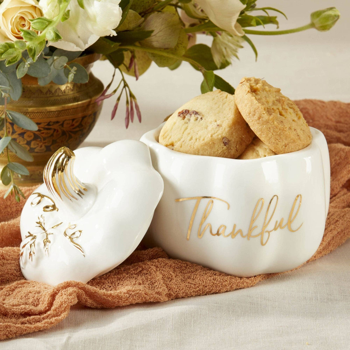 White ceramic containers with 'Thankful' text, filled with cookies, on a textured surface with flowers in the background.