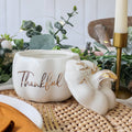 Decorative items on a table with 'Thankful' pot and white pumpkin with gold accents.