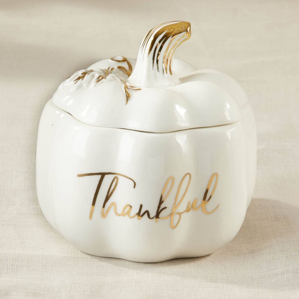 White ceramic pumpkin-shaped container with gold accents and 'Thankful' text on a beige background