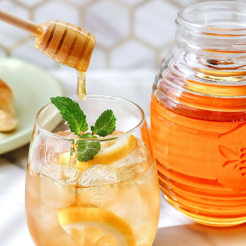 Glass of iced tea with lemon and mint, honeycomb drizzling honey, and a jar of honey on a light background.