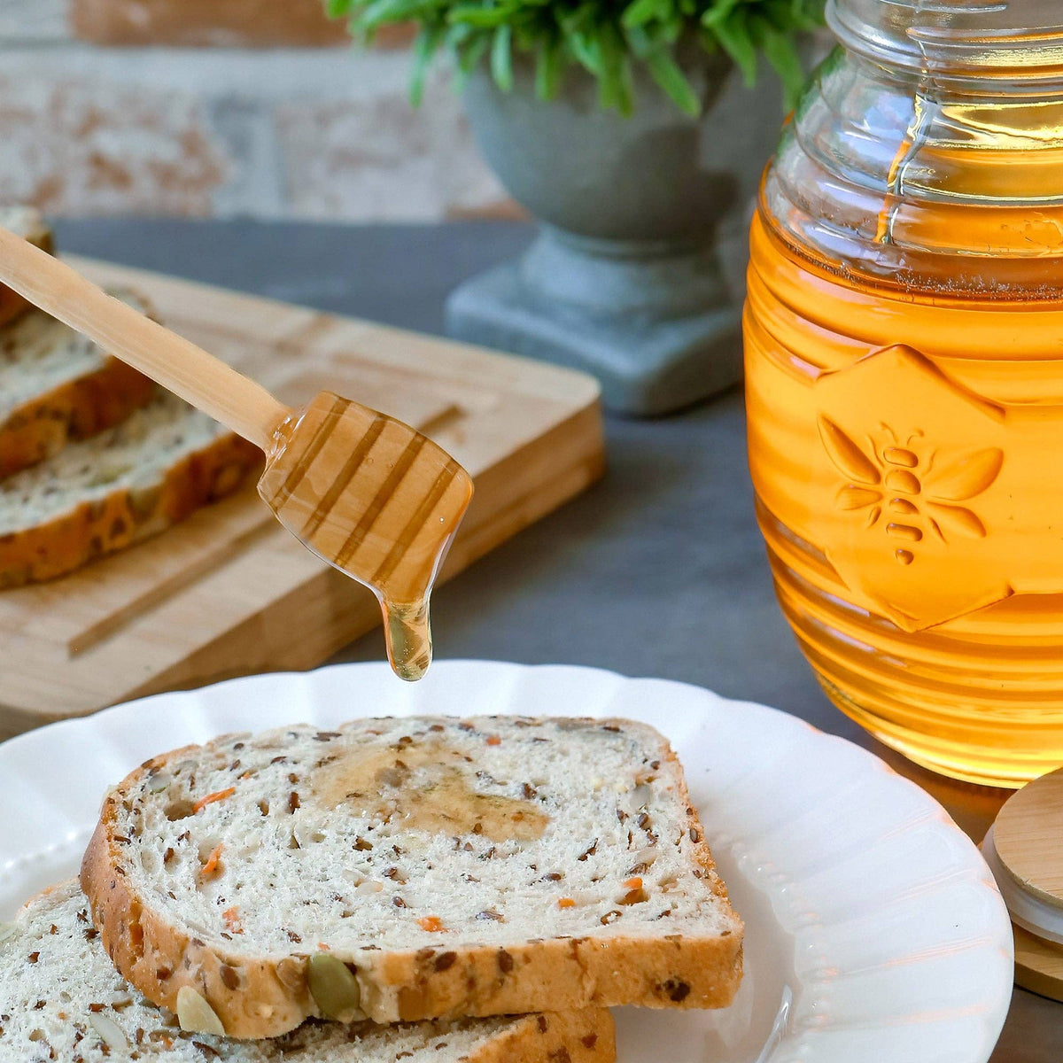 Honey jar with a wooden honey dipper over slices of bread on a plate, with a blurred background.
