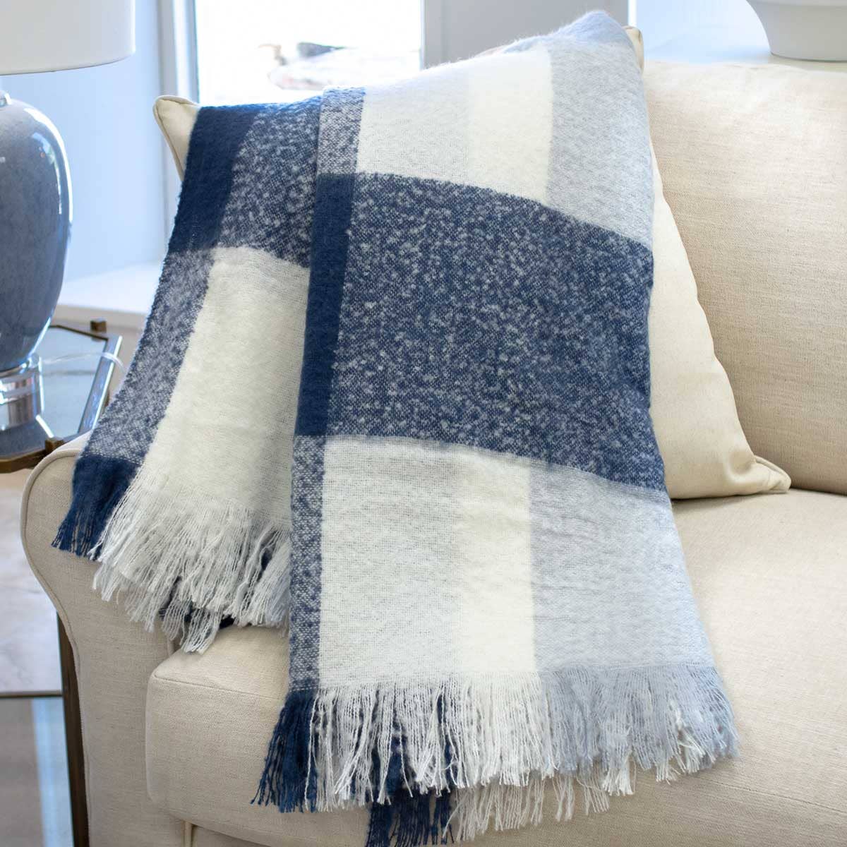 Blue and white checkered throw blanket with fringes on a beige couch.