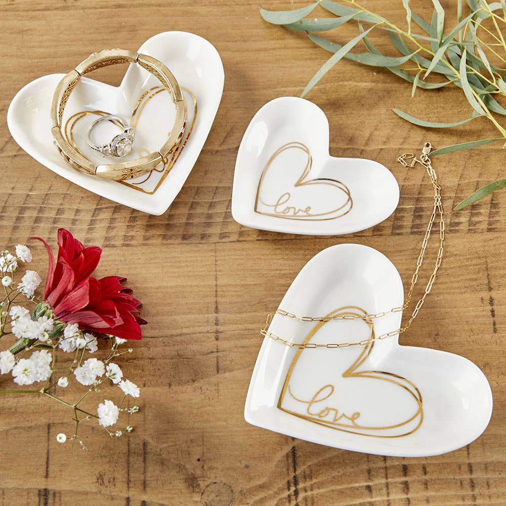 Heart-shaped ceramic dishes with gold 'love' engraving on a wooden surface with flowers and jewelry.