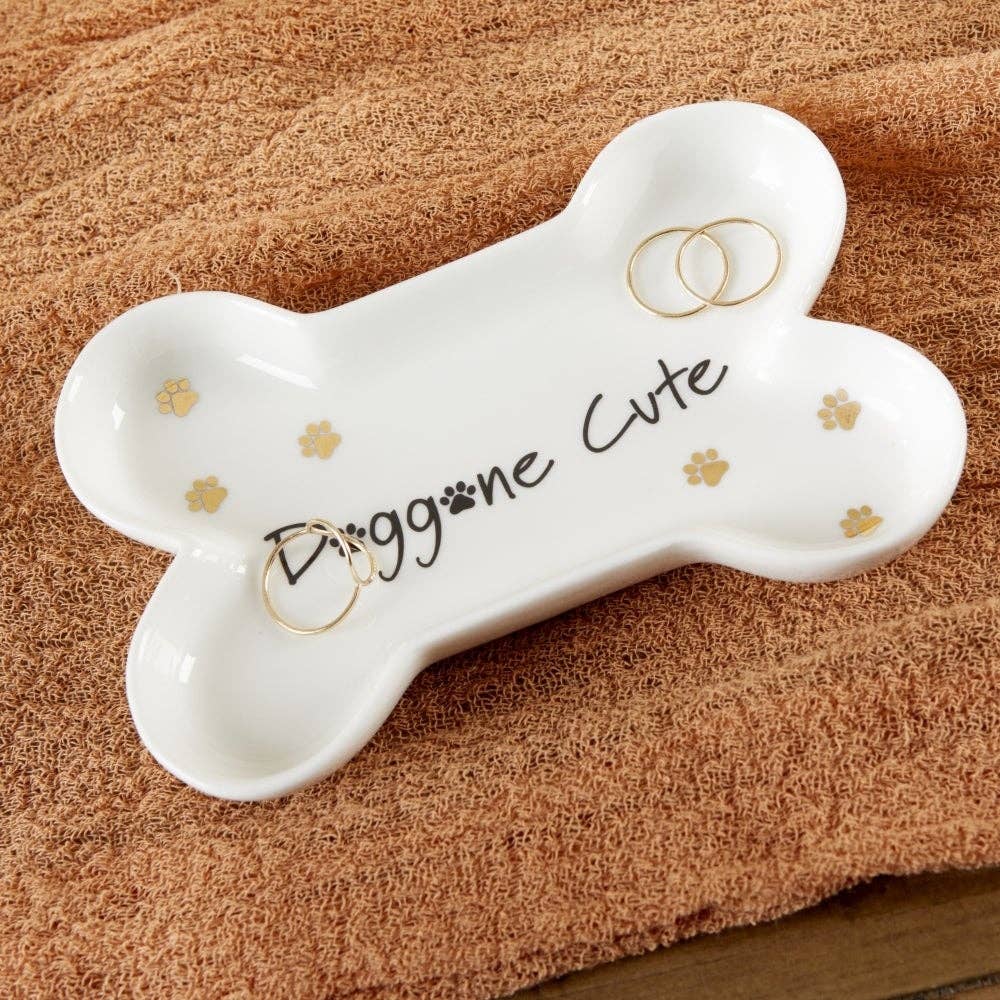 White bone-shaped ring holder with 'Doggone Cute' text on a brown textured surface