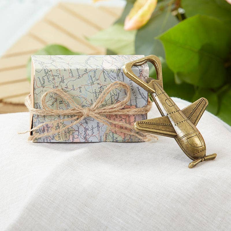Gift box with map design and airplane-shaped bottle opener on a white surface with green leaves in the background
