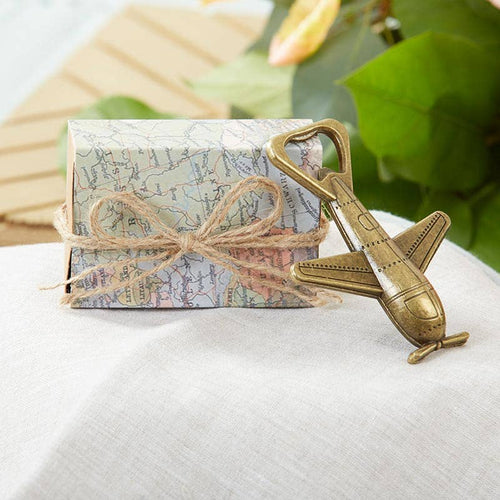 Gift box with map design and airplane-shaped bottle opener on a white surface with green leaves in the background