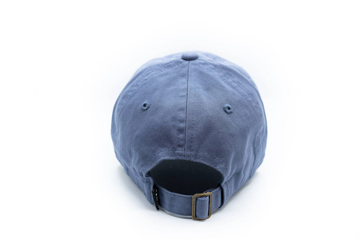 A blue cotton baseball cap shown from the back, featuring an adjustable strap with a brass buckle, on a solid white background.