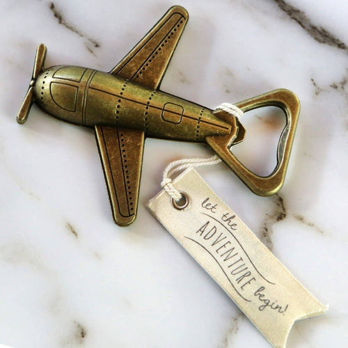 Brass airplane-shaped bottle opener with 'let the adventure begin' tag on marble surface