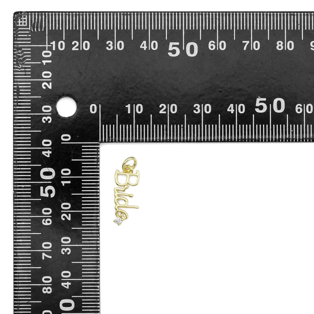 Gold charm with a diamond on a black ruler for size reference