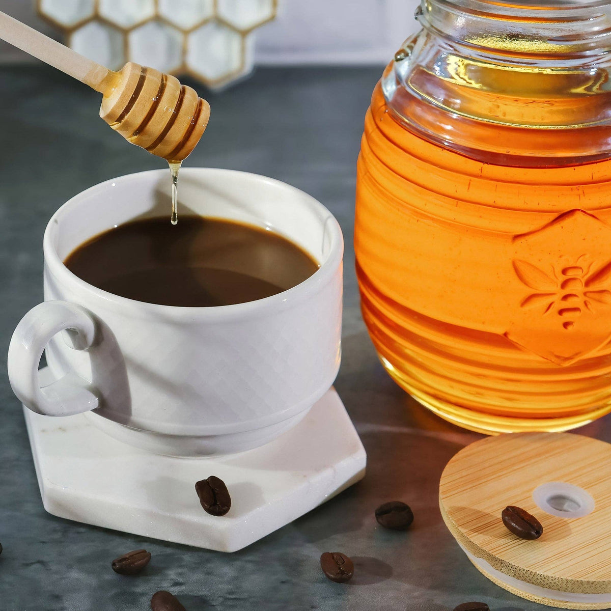 White mug with coffee, honey jar, and honey dipper on a dark surface.