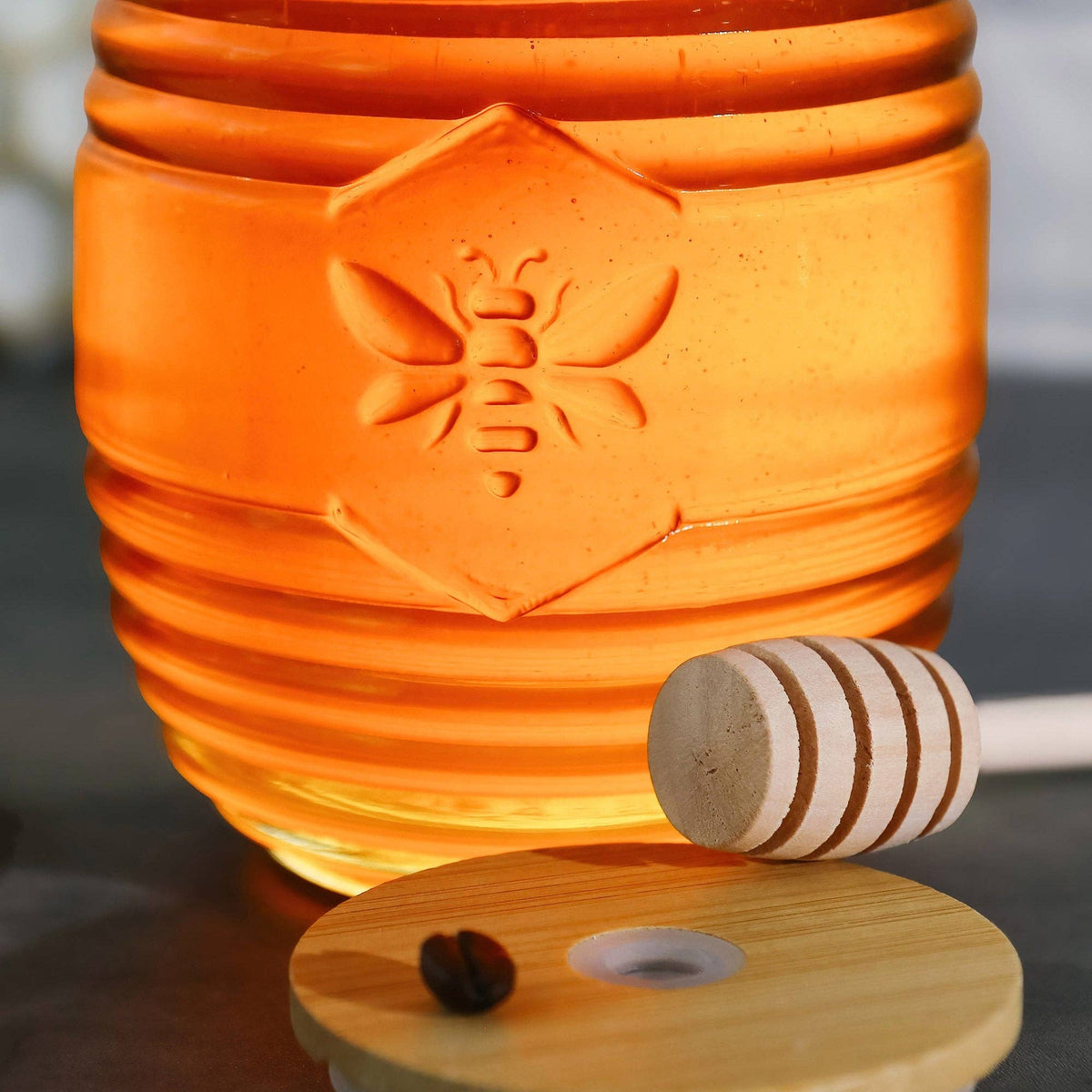 Honey jar with a wooden dipper and honeycomb on a reflective surface